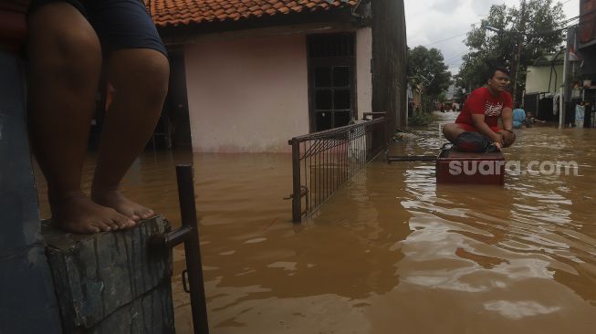 Dokumentasi - Warga beraktivitas saat banjir merendam Kelurahan Cipinang Melayu, Jakarta, Jumat (19/2/2021). [Suara.com/Angga Budhiyanto]