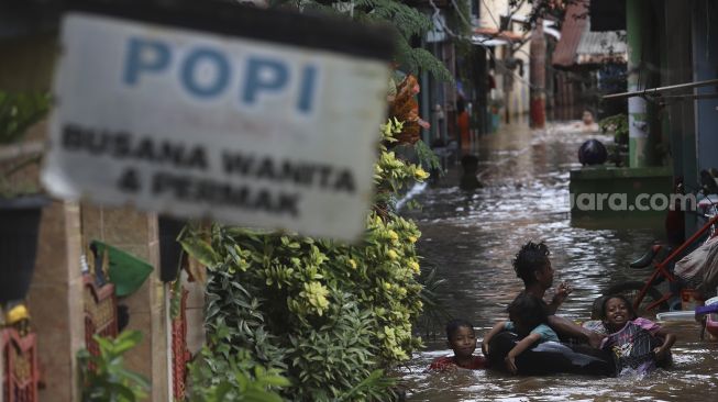Sejumlah anak bermain air saat banjir merendam Kelurahan Cipinang Melayu, Jakarta, Jumat (19/2/2021). [Suara.com/Angga Budhiyanto]