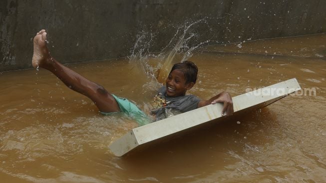 Seorang anak bermain air saat banjir merendam Kelurahan Cipinang Melayu, Jakarta, Jumat (19/2/2021). [Suara.com/Angga Budhiyanto]