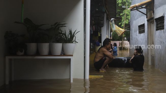 Warga beraktivitas di depan rumahnya yang terendam banjir di Cipinang Muara, Jakarta, Jumat (19/2/2021). [Suara.com/Angga Budhiyanto]