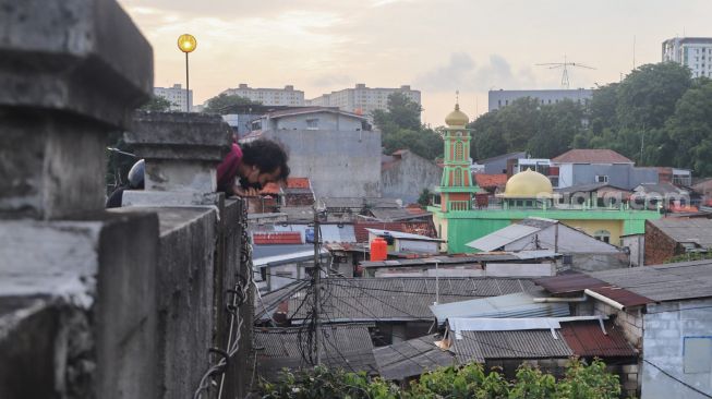 Seorang warga menonton banjir dan aliran kali Ciliwung yang meluap dari atas Flyover Kalibata, Jakarta Selatan, Sabtu (20/2/2021). [Suara.com/Alfian Winanto]