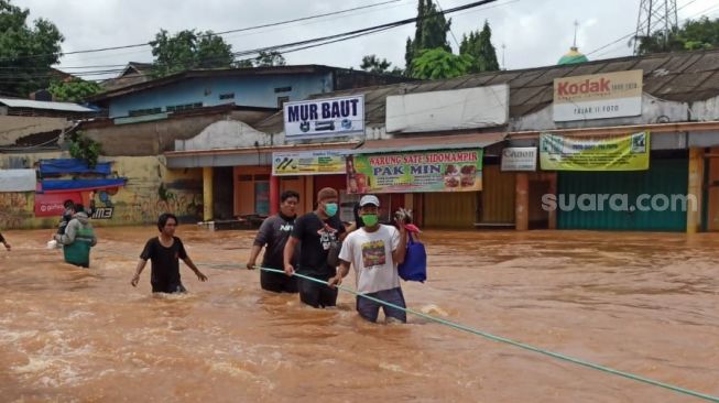 Warga tengah menerjang banjir Bekasi, Sabtu (20/2/2021).[Suara.com/Imam Faishal]