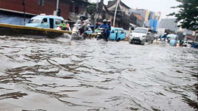 Suasana arus lalu lintas di Jalan Jatinegara Barat, Jakarta Timur yang tersendat akibat sebagian badan jalan terendam banjir luapan Sungai Ciliwung dengan ketinggian sekitar 20 sentimeter, Sabtu (20/2). [Suara.com/Oke Atmaja]
