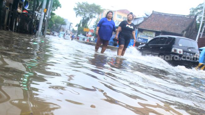 Warga melintas di Jalan Jatinegara Barat, Jakarta Timur yang tersendat akibat sebagian badan jalan terendam banjir luapan Sungai Ciliwung dengan ketinggian sekitar 20 sentimeter, Sabtu (20/2). [Suara.com/Oke Atmaja]
