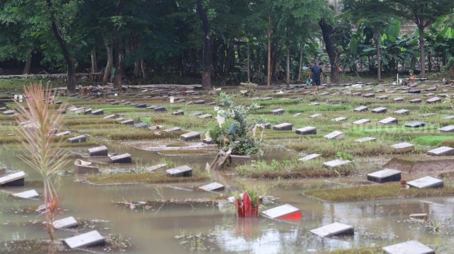 Petugas beraktivitas di sekitar area makam yang terendam banjir di TPU Jeruk Purut, Jakarta Selatan, Sabtu (20/2/2021). [Suara.com/Alfian Winanto]