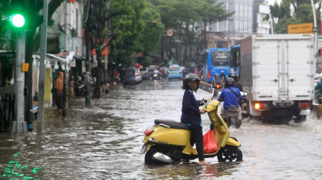 Pengendara melintas di Jalan Jatinegara Barat, Jakarta Timur yang tersendat akibat sebagian badan jalan terendam banjir luapan Sungai Ciliwung dengan ketinggian sekitar 20 sentimeter, Sabtu (20/2). [Suara.com/Oke Atmaja]
