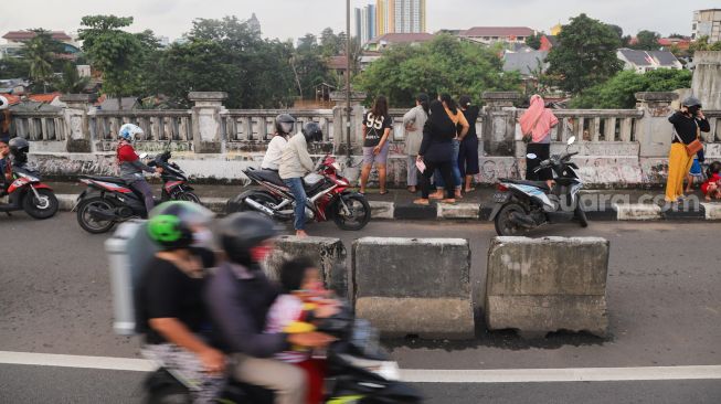 Sejumlah warga dan pengendara motor menonton banjir dan aliran kali Ciliwung yang meluap dari atas Flyover Kalibata, Jakarta Selatan, Sabtu (20/2/2021). [Suara.com/Alfian Winanto]