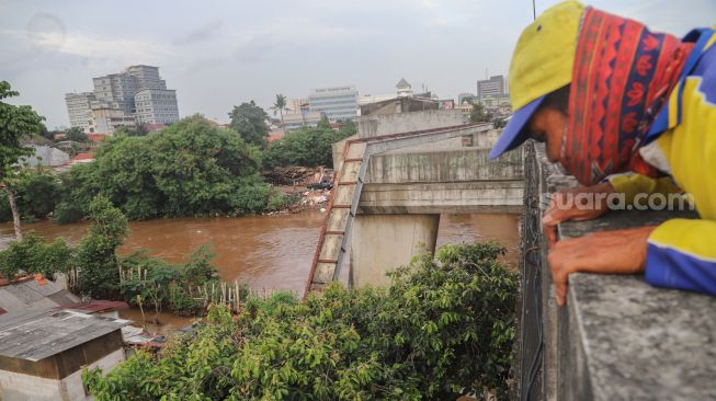 Seorang warga menonton banjir dan aliran kali Ciliwung yang meluap dari atas Flyover Kalibata, Jakarta Selatan, Sabtu (20/2/2021). [Suara.com/Alfian Winanto]