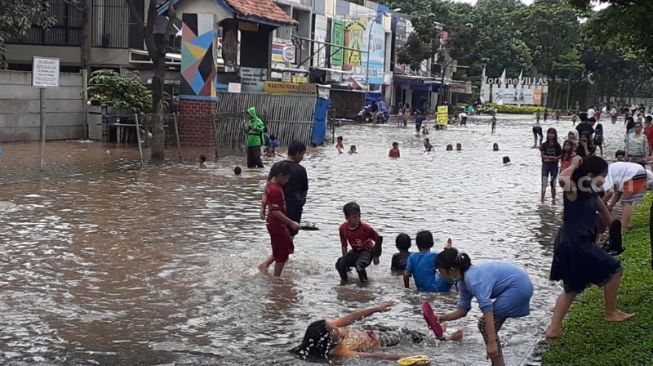 Sejumlah orangtua dan anak-anak tampak asyik berenang di lokasi banjir di Ruko Fortune, Jalan Graha Boulevard Raya, Paku Jaya, Serpong Utara, Tangsel, Sabtu (20/2/2021). [Suara.com/Wivy]