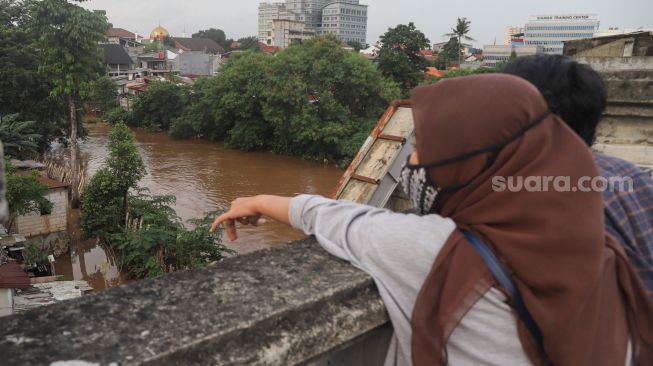 Warga menonton banjir dan aliran kali Ciliwung yang meluap dari atas Flyover Kalibata, Jakarta Selatan, Sabtu (20/2/2021). [Suara.com/Alfian Winanto]