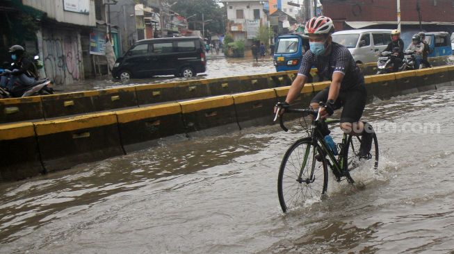 Pesepeda melintas di Jalan Jatinegara Barat, Jakarta Timur yang tersendat akibat sebagian badan jalan terendam banjir luapan Sungai Ciliwung dengan ketinggian sekitar 20 sentimeter, Sabtu (20/2). [Suara.com/Oke Atmaja]
