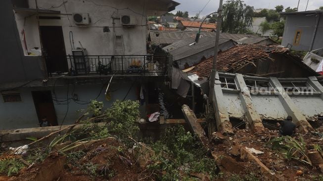 Warga membersihkan puing-puing reruntuhan di rumahnya yang tertimpa tanah longsor di Kelurahan Bangka, Mampang Prapatan, Jakarta, Minggu (21/2/2021). [Suara.com/Angga Budhiyanto]