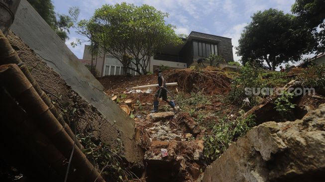 Warga membersihkan puing-puing reruntuhan di rumahnya yang tertimpa tanah longsor di Kelurahan Bangka, Mampang Prapatan, Jakarta, Minggu (21/2/2021). [Suara.com/Angga Budhiyanto]