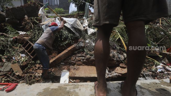 Warga membersihkan puing-puing reruntuhan di rumahnya yang tertimpa tanah longsor di Kelurahan Bangka, Mampang Prapatan, Jakarta, Minggu (21/2/2021). [Suara.com/Angga Budhiyanto]