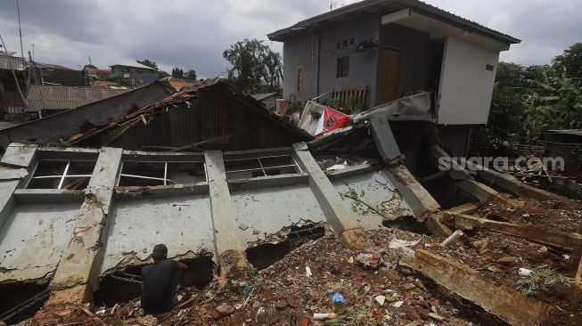 Warga membersihkan puing-puing reruntuhan di rumahnya yang tertimpa tanah longsor di Kelurahan Bangka, Mampang Prapatan, Jakarta, Minggu (21/2/2021). [Suara.com/Angga Budhiyanto]