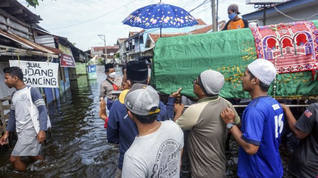 Sejumlah warga bergotong royong membawa peti jenazah orang meninggal yang akan dimakamkan melewati jalan yang tergenang banjir di Tempat Pemakaman Umum (TPU), Pekalongan, Jawa Tengah, Minggu (21/2/2021). [ANTARA FOTO/Harviyan Perdana Putra]