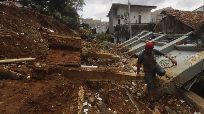 Warga berjalan melintasi puing-puing reruntuhan akibat tanah longsor di Kelurahan Bangka, Mampang Prapatan, Jakarta, Minggu (21/2/2021). [Suara.com/Angga Budhiyanto]