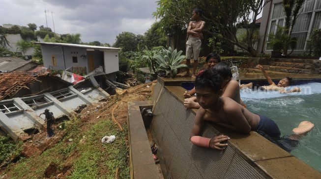 Sejumlah anak berenang di dekat lokasi tanah longsor yang menimpa rumah warga di Kelurahan Bangka, Mampang Prapatan, Jakarta, Minggu (21/2/2021). [Suara.com/Angga Budhiyanto]