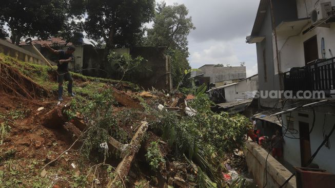 Warga membersihkan puing-puing reruntuhan di rumahnya yang tertimpa tanah longsor di Kelurahan Bangka, Mampang Prapatan, Jakarta, Minggu (21/2/2021). [Suara.com/Angga Budhiyanto]