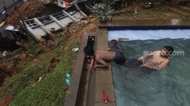 Sejumlah anak berenang di dekat lokasi tanah longsor yang menimpa rumah warga di Kelurahan Bangka, Mampang Prapatan, Jakarta, Minggu (21/2/2021). [Suara.com/Angga Budhiyanto]