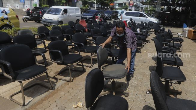 Seorang karyawan menata kursi yang dikeringkan di salah satu bank di kawasan Kemang, Jakarta, Senin (22/2/2021). [Suara.com/Angga Budhiyanto]