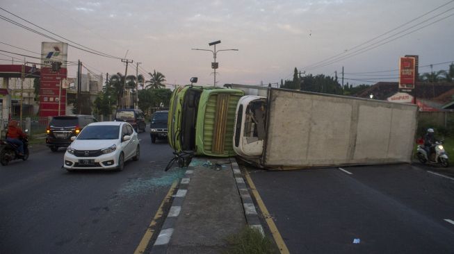 Sejumlah kendaraan melintas di dekat truk pengangkut barang kemasan yang terguling di Jalur Pantura, Desa Cibanggala, Subang, Jawa Barat, Minggu (21/2/2021). . ANTARA FOTO/M Ibnu Chazar
