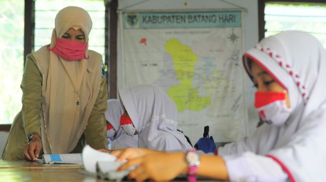 Guru memberikan materi pelajaran kepada siswa sambil mengenakan masker saat hari pertama dimulainya kembali pembelajaran tatap muka di SDN 82/I Serasah, Batanghari, Jambi, Senin (22/2/2021). ANTARA FOTO/Wahdi Septiawan