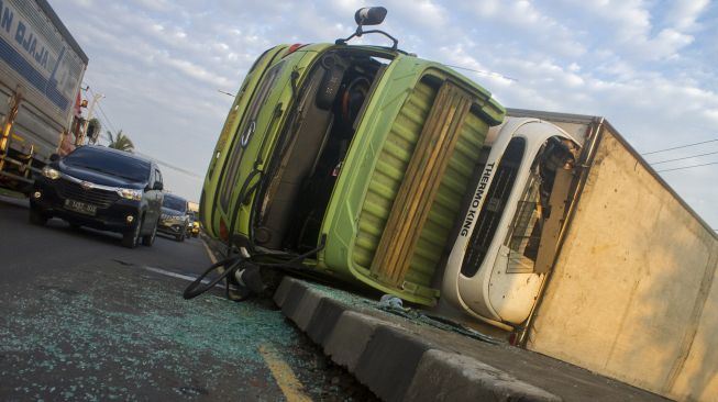 Sejumlah kendaraan melintas di dekat truk pengangkut barang kemasan yang terguling di Jalur Pantura, Desa Cibanggala, Subang, Jawa Barat, Minggu (21/2/2021). . ANTARA FOTO/M Ibnu Chazar
