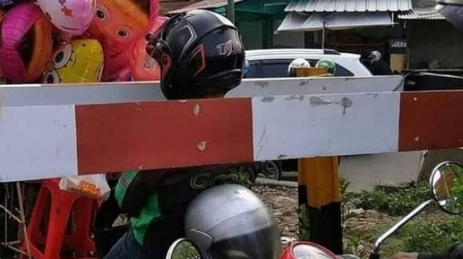 Kepala ojol tersangkut di palang pintu rel kereta. (Instagram)