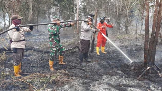 Kapolres Siak AKBP Gunar Rahardyanto, Kadaops Manggala Agni Siak Ihsan Abdillah, dan TNI saat memadamkan api di Kecamatan Sungai Apit, Kabupaten Siak. [Suara.com/Alfat Handri]