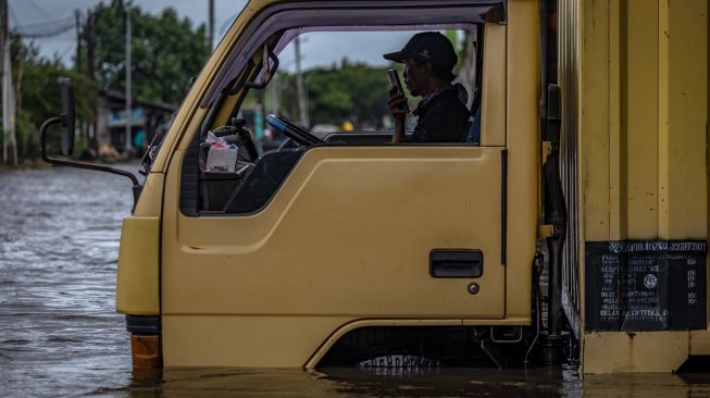 Seorang sopir menghubungi rekannya setelah truknya mogok terjebak banjir yang merendam Jalur Pantura Kaligawe-Genuk, Semarang, Jawa Tengah, Rabu (24/2/2021).  ANTARA FOTO/Aji Styawan