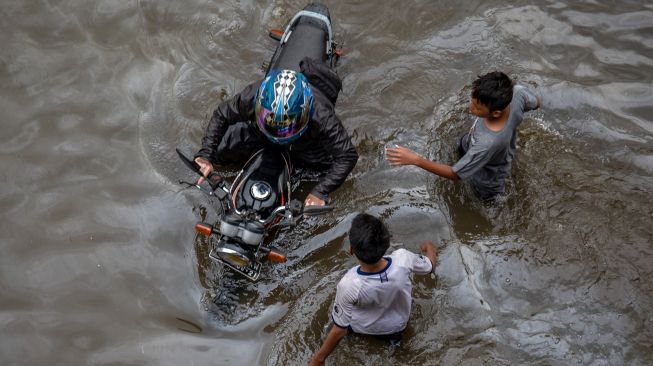 Seorang warga mendorong motornya yang mogok karena nekat menembus banjir yang merendam Jalur Pantura Kaligawe-Genuk, Semarang, Jawa Tengah, Rabu (24/2/2021). ANTARA FOTO/Aji Styawan