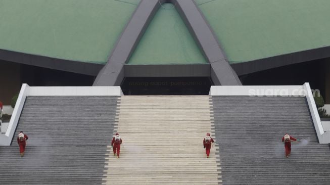 Petugas pemadam kebakaran menyemprotkan cairan disinfektan di area komplek Gedung DPR/MPR RI, Jakarta, Minggu (9/8/2020). [Suara.com/Angga Budhiyanto]