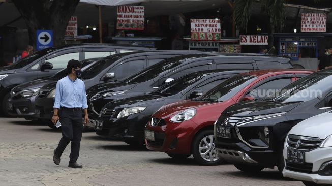 Warga berjalan melintasi deretan mobil yang terparkir di pelataran parkir IRTI Monas, Jakarta, Selasa (2/3/2021). [Suara.com/Angga Budhiyanto]