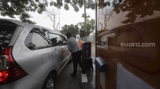 Petugas Dinas Perhubungan (Dishub) memberikan tiket parkir kepada pengendara mobil yang akan memarkirkan kendaraannya di pelataran parkir IRTI Monas, Jakarta, Selasa (2/3/2021). [Suara.com/Angga Budhiyanto]