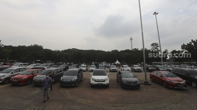 Warga berjalan melintasi deretan mobil yang terparkir di pelataran parkir IRTI Monas, Jakarta, Selasa (2/3/2021). [Suara.com/Angga Budhiyanto]