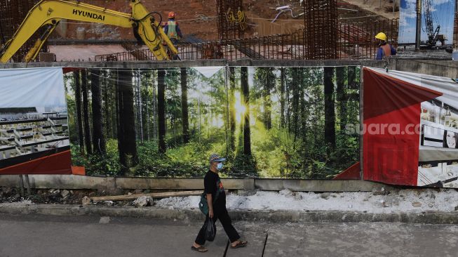 Warga berjalan di samping proyek pembangunan Pasar Senen Jaya Blok I dan II, Jakarta, Kamis (4/3/2021). [Suara.com/Angga Budhiyanto]