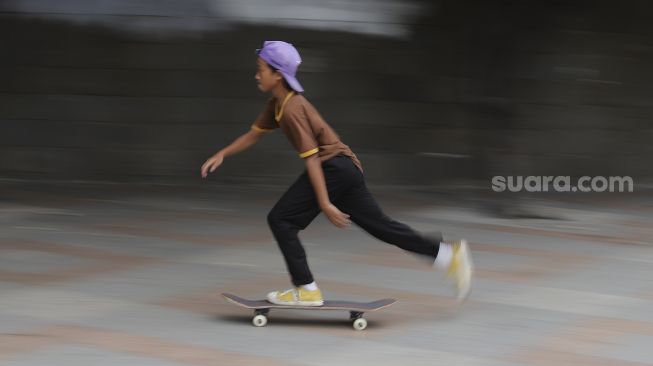 Seorang anak bermain papan luncur (skateboard) di trotoar kawasan Bundaran HI, Jakarta, Jumat (5/3/2021). [Suara.com/Angga Budhiyanto]