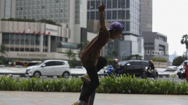 Seorang anak bermain papan luncur (skateboard) di trotoar kawasan Bundaran HI, Jakarta, Jumat (5/3/2021). [Suara.com/Angga Budhiyanto]