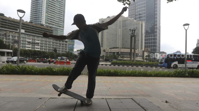 Seorang anak bermain papan luncur (skateboard) di trotoar kawasan Bundaran HI, Jakarta, Jumat (5/3/2021). [Suara.com/Angga Budhiyanto]