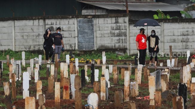 Warga berziarah ke makam kerabatnya di area khusus pemakaman Covid-19 yang terisi penuh di TPU Bambu Apus , Jakarta Timur, Sabtu (6/3/2021). [Suara.com/Alfian Winanto]