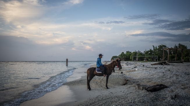 Seorang penyedia jasa kuda menaiki kudanya saat menanti kunjungan wisatawan di Gili Trawangan, Kepulauan Gili, Lombok Utara, Nusa Tenggara Barat, Sabtu (6/3/2021). [ANTARA FOTO/Aprillio Akbar]