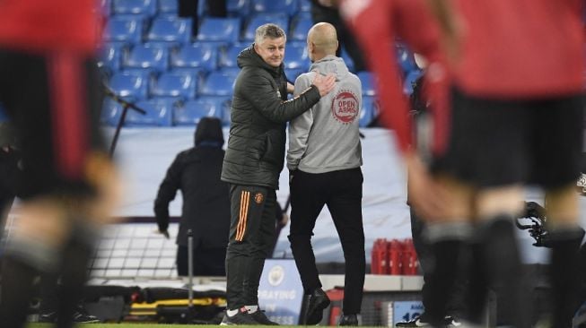 Manajer Manchester United, Ole Gunnar Solskjaer (kiri) berinteraksi dengan manajer Manchester City, Pep Guardiola seusai laga Liga Inggris 2020/2021 di Etihad Stadium, Manchester, Minggu (8/3/2021) dini hari WIB. [PETER POWELL / POOL / AFP]