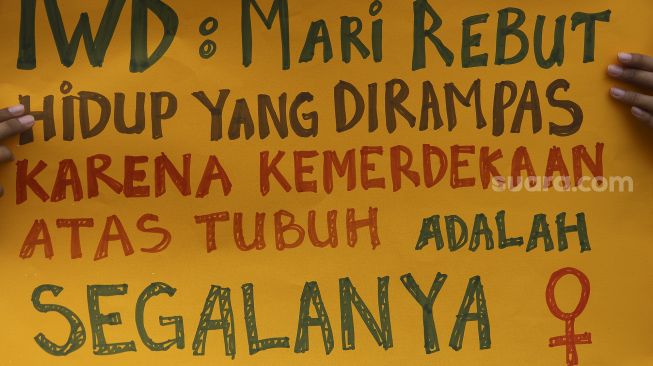 Seorang massa yang tergabung dalam Perempuan Mahardhika membawa poster saat melakukan aksi memperingati Hari Perempuan Internasional di kawasan Patung Kuda Arjuna Wiwaha, Jakarta, Senin (8/3/2021). [Suara.com/Angga Budhiyanto]