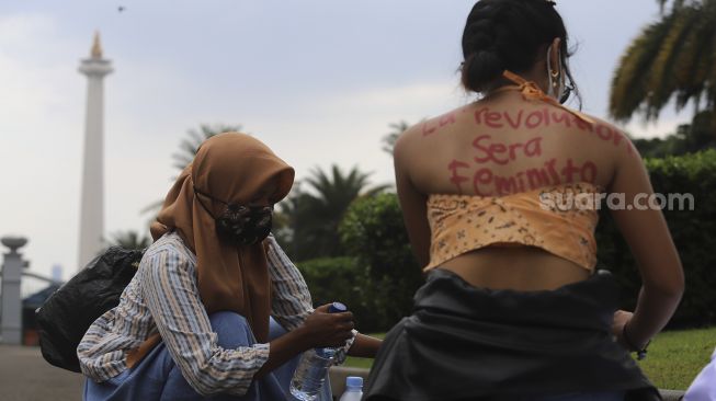 Seorang massa yang tergabung dalam Perempuan Mahardhika membeli air mineral si sela-sela melakukan aksi memperingati Hari Perempuan Internasional di kawasan Patung Kuda Arjuna Wiwaha, Jakarta, Senin (8/3/2021). [Suara.com/Angga Budhiyanto]