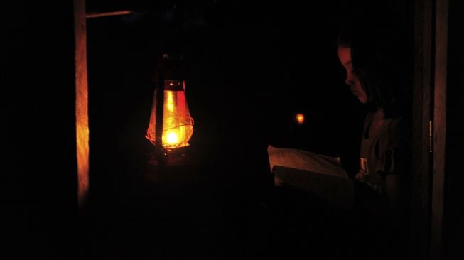 Seorang anak membaca hanya diterangi lampu minyak di rumahnya yang belum mendapatkan layanan listrik di Kampung Jao, Nagari Panyubarangan, Dharmasraya, Sumatera Barat, Senin (8/3/2021).  ANTARA FOTO/Wahdi Septiawan