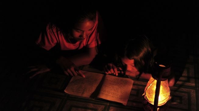 Dua anak membaca hanya diterangi lampu minyak di rumahnya yang belum mendapatkan layanan listrik di Kampung Jao, Nagari Panyubarangan, Dharmasraya, Sumatera Barat, Senin (8/3/2021).  ANTARA FOTO/Wahdi Septiawan