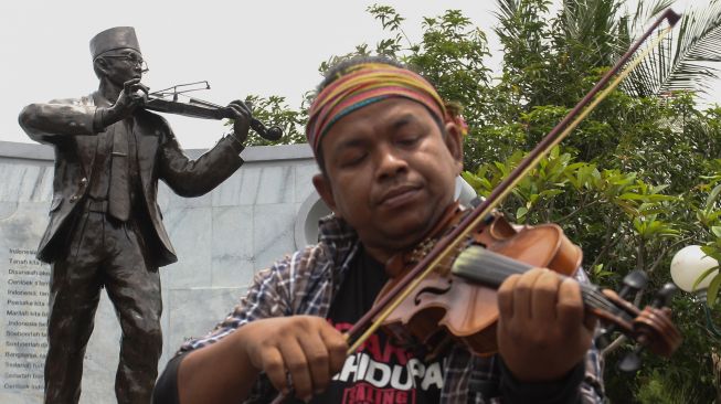 Warga memainkan biola saat berziarah, di komplek makam WR Soepratman di Surabaya, Jawa Timur, Selasa (9/3/2021). ANTARA FOTO/Didik Suharton