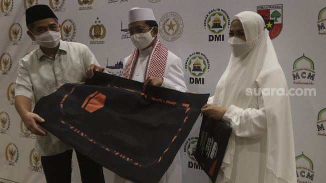 Chairman Indika Foundation Arsjad Rasjid (kiri) didampingi Ketua Badan Pengusaha Pemuda Pancasila Mufrina (kanan) menyerahkan sajadah pelindung COVID-19 kepada Imam Besar Masjid Istiqlal KH. Nasaruddin Umar (tengah) dalam acara peluncuran "Gerakan Nasional Mengisi Masjid dengan 1 Juta Sajadah Pelindung COVID-19" di Masjid Istiqlal, Jakarta, Kamis (11/3/2021). [Suara.com/Angga Budhiyanto]