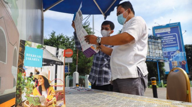 Petugas Dinas Pariwisata dan Ekonomi Kreatif DKI Jakarta menjelaskan tentang destinasi wisata kepada warga saat uji coba Tourist Information Center Mobile (TICM) di Terminal Blok M, Jakarta Selatan, Jumat (12/3/2021). [Suara.com/Alfian Winanto]